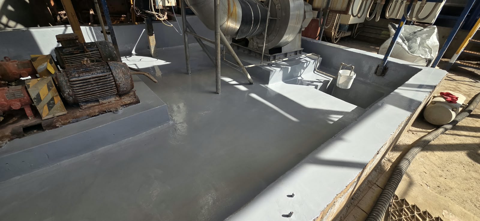 Pretil de contención secundaria en planta industrial, revestido con un recubrimiento polimérico gris liso para protección contra ataques químicos y filtraciones.