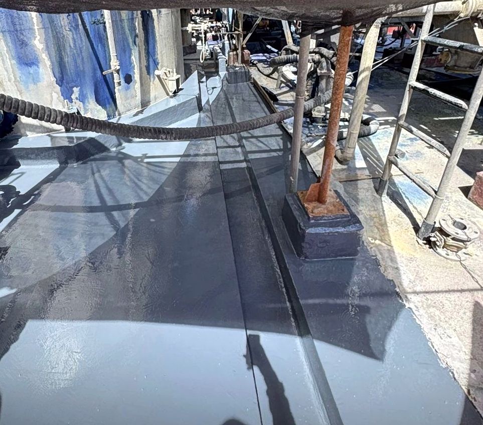 Canaleta y piso de contención industrial impermeabilizados con recubrimiento polimérico gris uniforme, en entorno industrial con mangueras y estructuras metálicas.