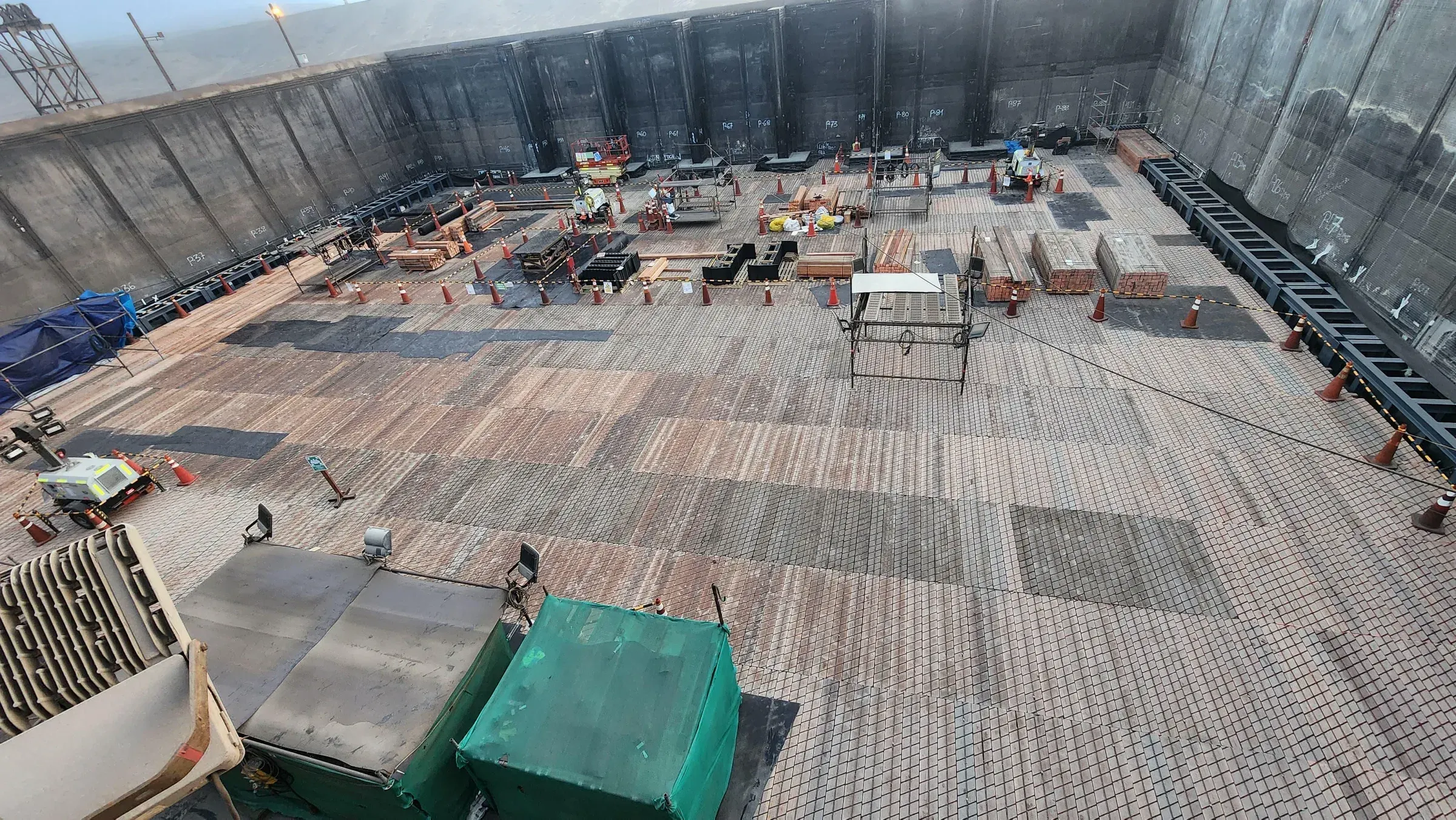 Piso e interior de un gran estanque o fosa de contención industrial en mantenimiento, con conos de seguridad, andamios y equipos de trabajo en faena minera.