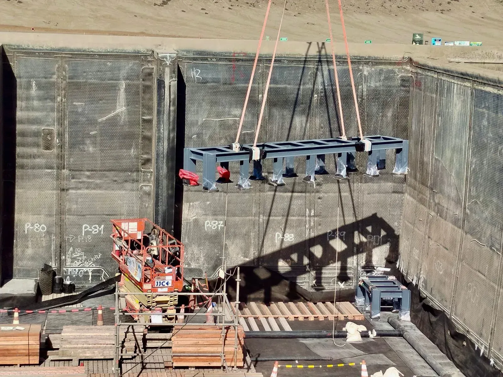 Izamiento y maniobra de una estructura metálica con recubrimiento protector gris, siendo posicionada mediante grúa dentro de una fosa industrial revestida en sitio minero.