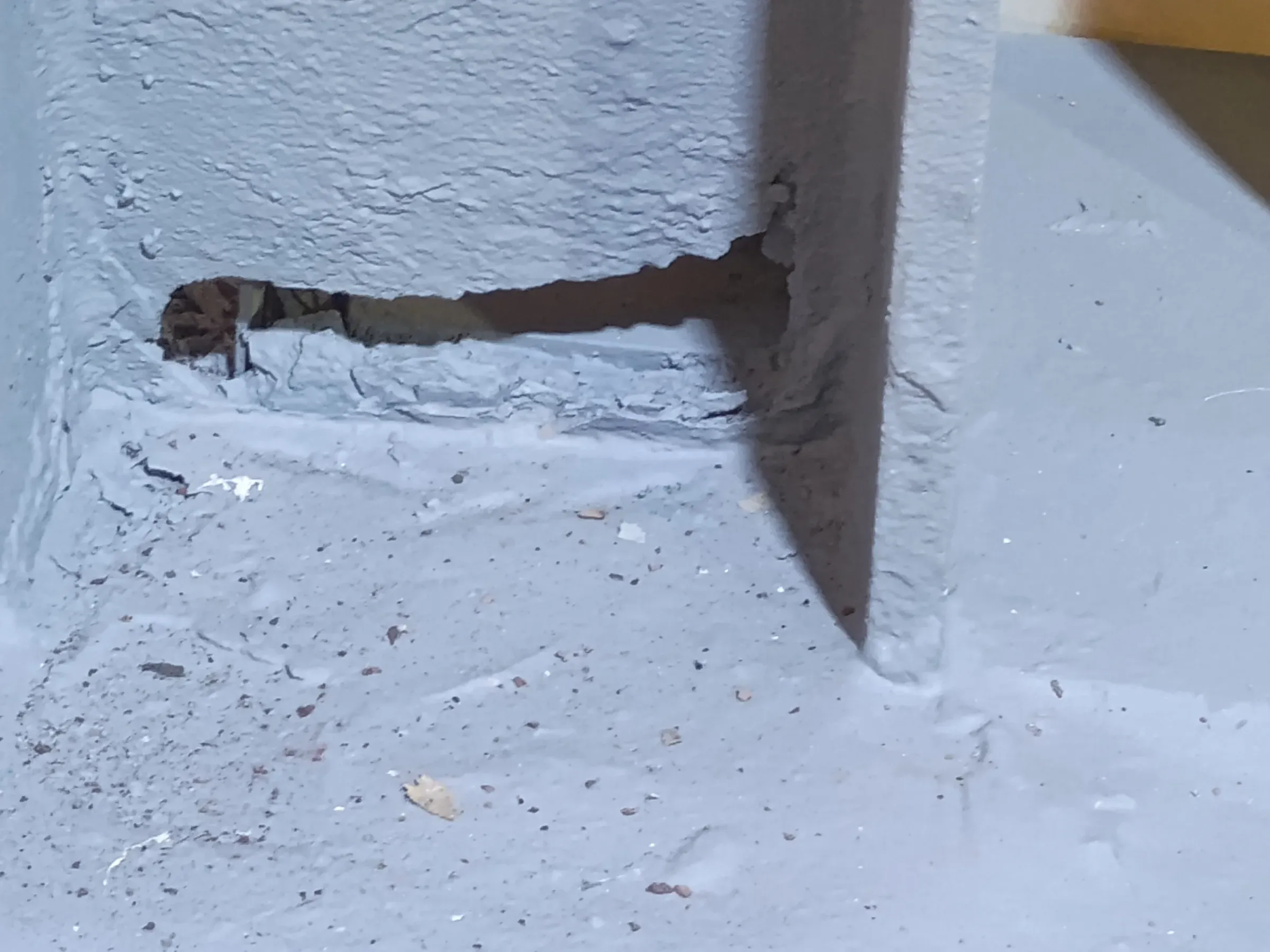 Base de viga estructural de acero con recubrimiento gris que presenta perforación por corrosión severa y pérdida de material en la unión con el piso.