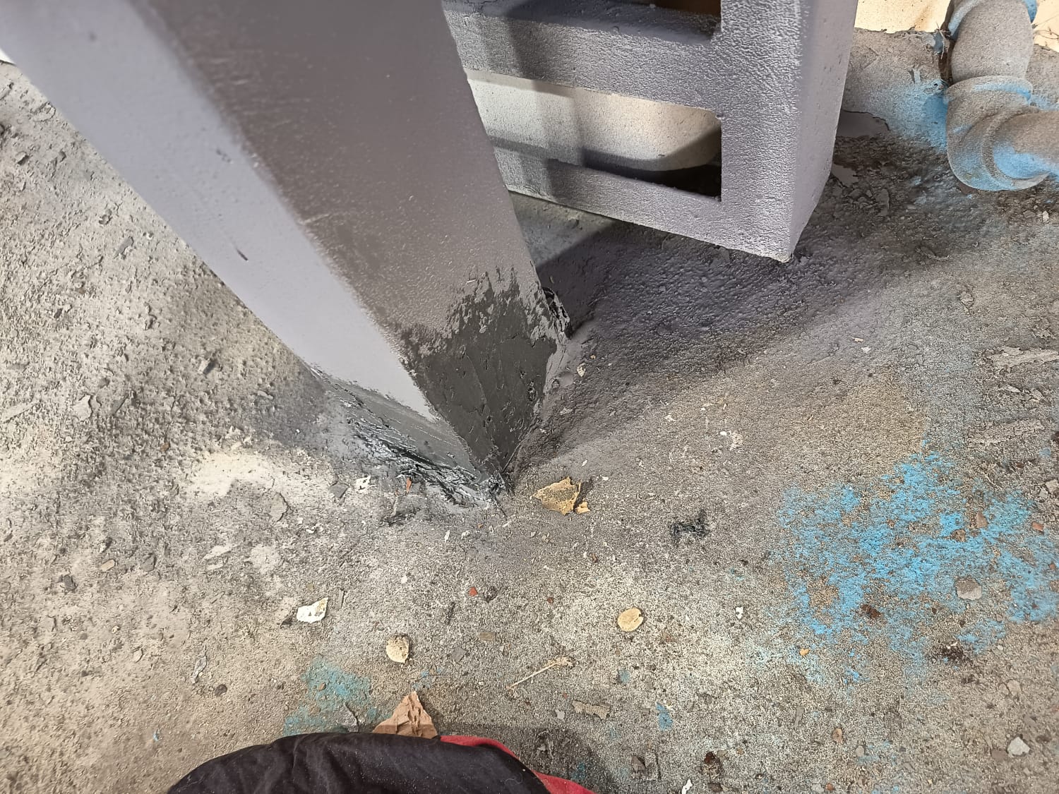 Base de pilar metálico estructural sellada con recubrimiento polimérico gris oscuro en la junta con el piso de hormigón para prevenir filtraciones y corrosión.