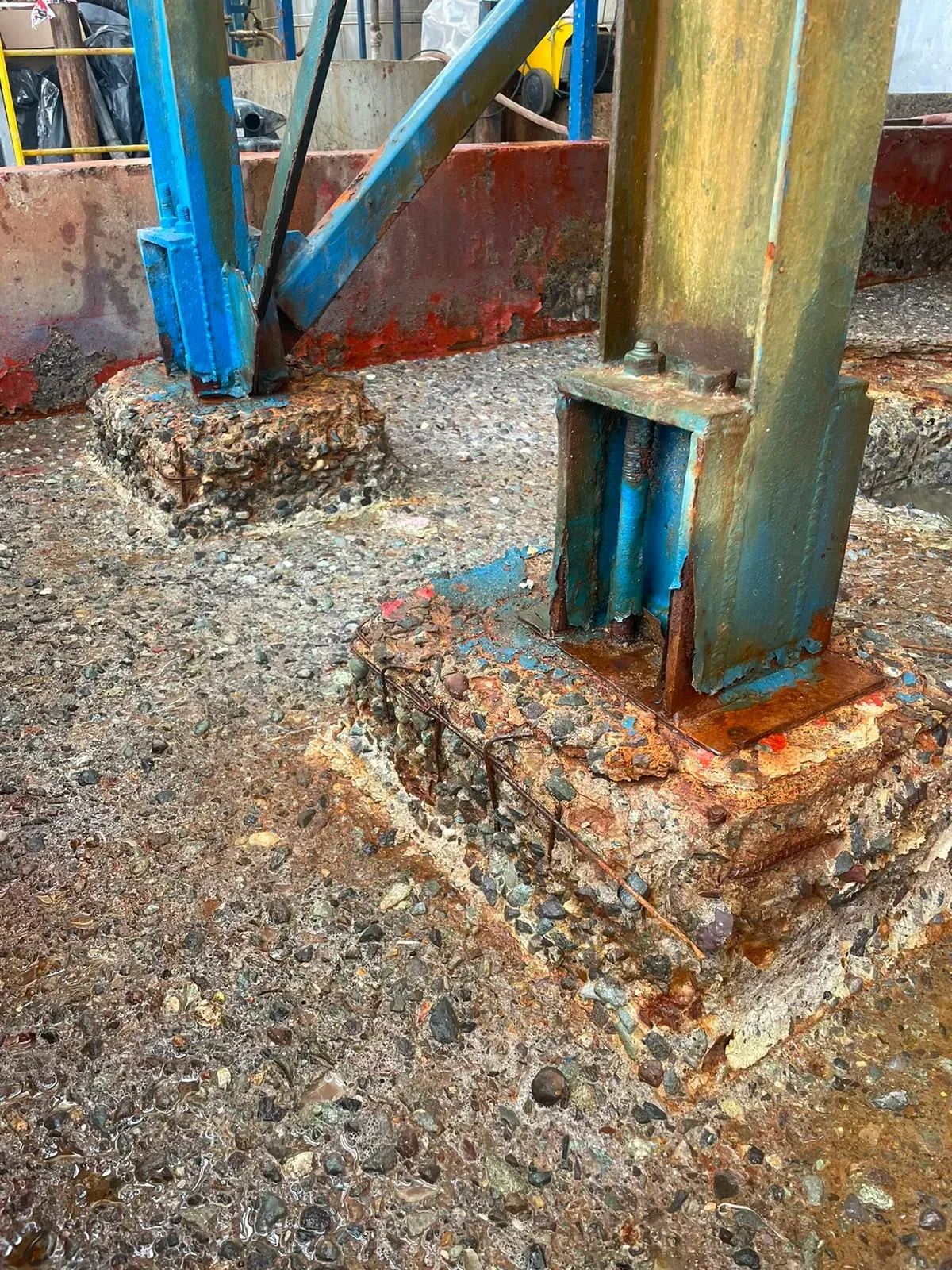 Columnas de acero estructural con severa corrosión en sus bases y pernos de anclaje, sobre pedestales de hormigón altamente degradados con enfierradura expuesta.