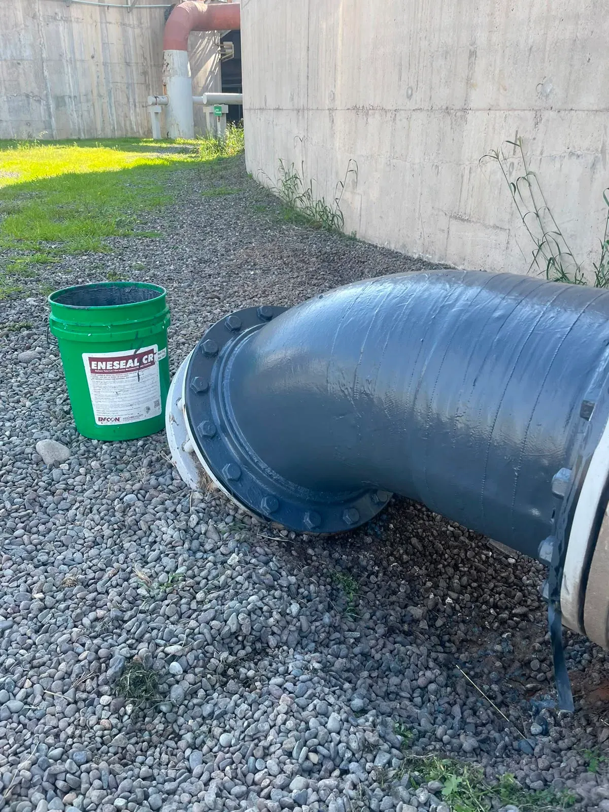 Codo de tubería industrial protegido con recubrimiento polimérico gris ENESEAL CR, ubicado en un entorno exterior sobre terreno de grava.
