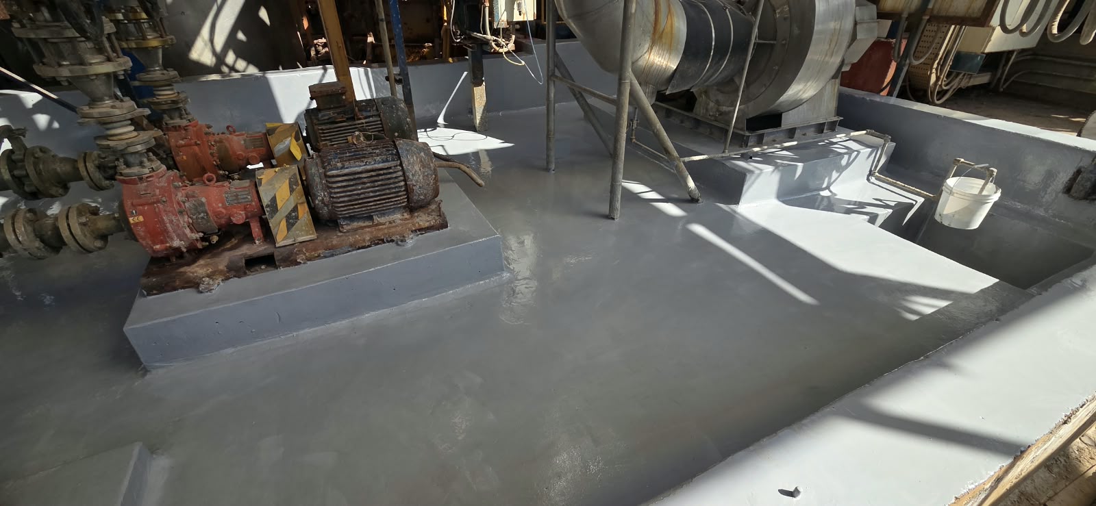 Pretil de contención de hormigón en planta industrial, protegido con un recubrimiento polimérico gris de alta resistencia química alrededor de bombas y motores.