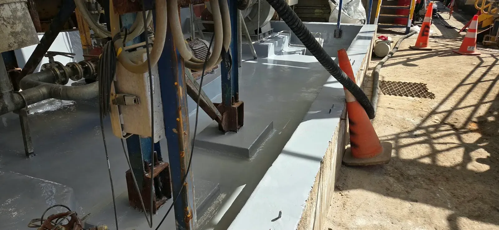 Pretil de contención de hormigón en planta industrial, recubierto con una capa polimérica gris lisa para protección química y control de derrames.