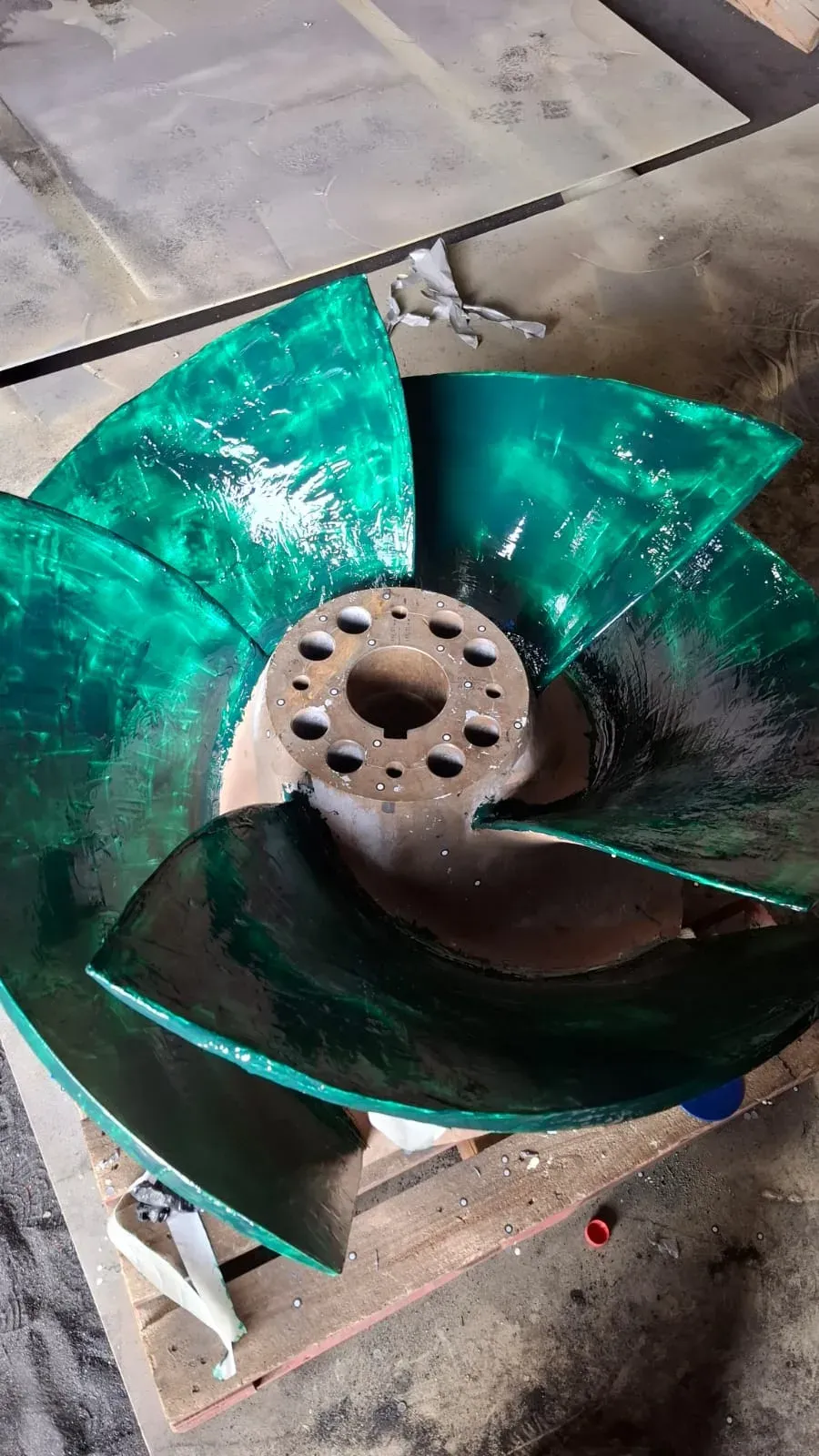 Impulsor industrial de cinco álabes recubierto con una capa polimérica protectora de color verde brillante, dispuesto sobre un palet de madera en un taller.